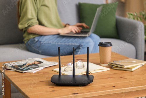 Modern wi-fi router on table of woman with laptop at home, closeup photo