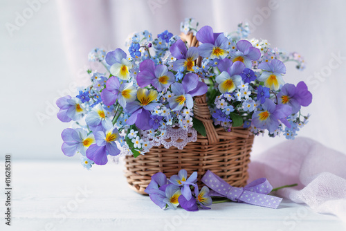 Spring forget-me-not flowers, viola pansy in a basket, bouquet with ribbon on a white table.