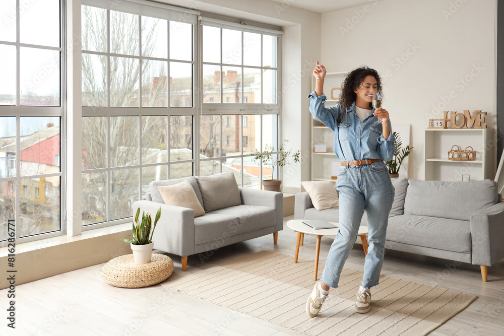 © Pixel-Shot - Young African-American woman with glass of champagne dancing at home