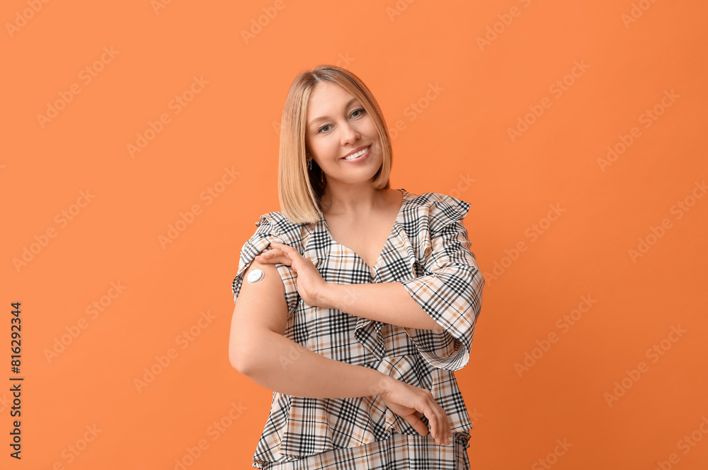 Woman with glucose sensor for measuring blood sugar level on orange background. Diabetes concept