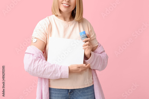 Woman with glucose sensor for measuring blood sugar level and blank paper on pink background. Diabetes concept