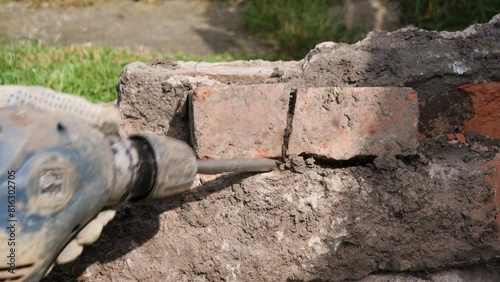 Male construction worker using an SDS impact drill power tool breaker with chisel bit to break bricks and mortar out of a concrete block by hand
