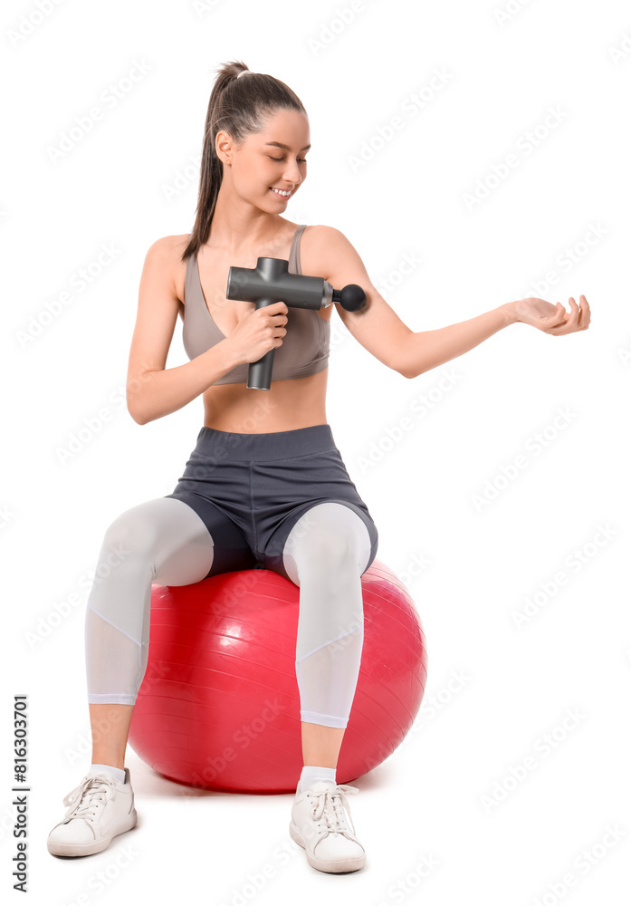 Sporty young woman massaging her arm with percussive massager on fitball against white background Sporty young woman massaging her arm with percussive massager on fitball against white background