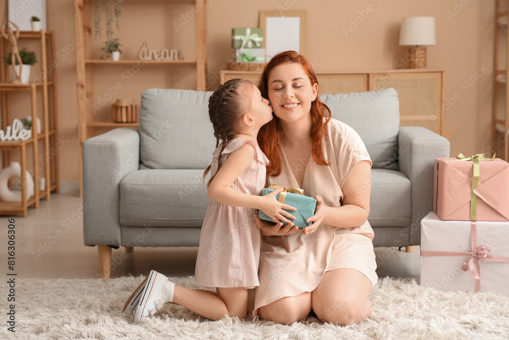 Girl kissing her mother and giving gift for Mother's Day in living room Girl kissing her mother and giving gift for Mother's Day in living room