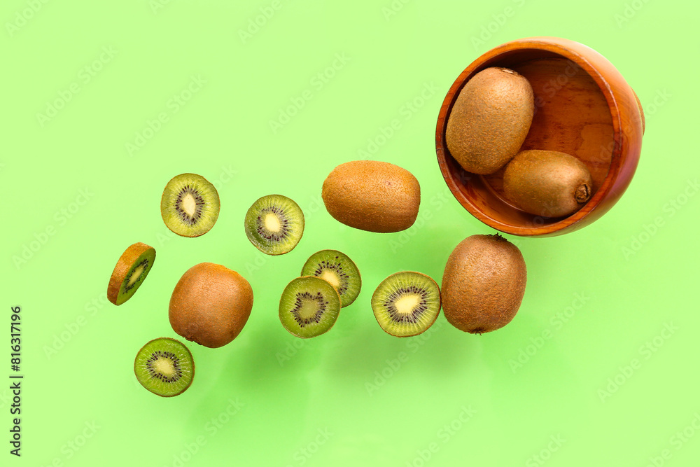 Wooden bowl with fresh kiwi flying on green background
