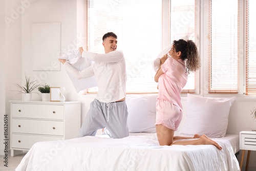 Happy young beautiful couple fighting pillows in bedroom