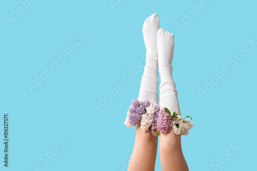 Legs of beautiful young woman in socks with lilac flowers on blue background