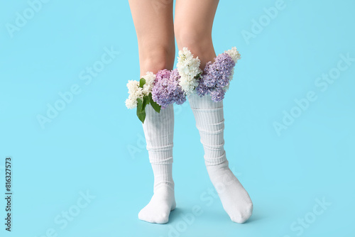 Legs of beautiful young woman in socks with lilac flowers on blue background