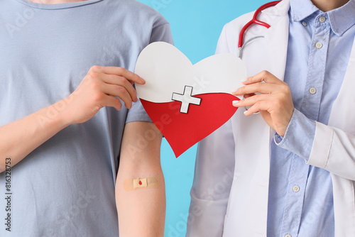 Male blood donor with doctor holding paper heart on blue background, closeup