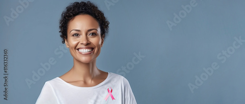 Banner Breast Cancer Awareness. Beautiful Smiling With White Teeth Woman In Her 50s with Pink Ribbon on White T-Shirt On Blue Background, Copy Space., Health. Ai Generated. Horizontal.