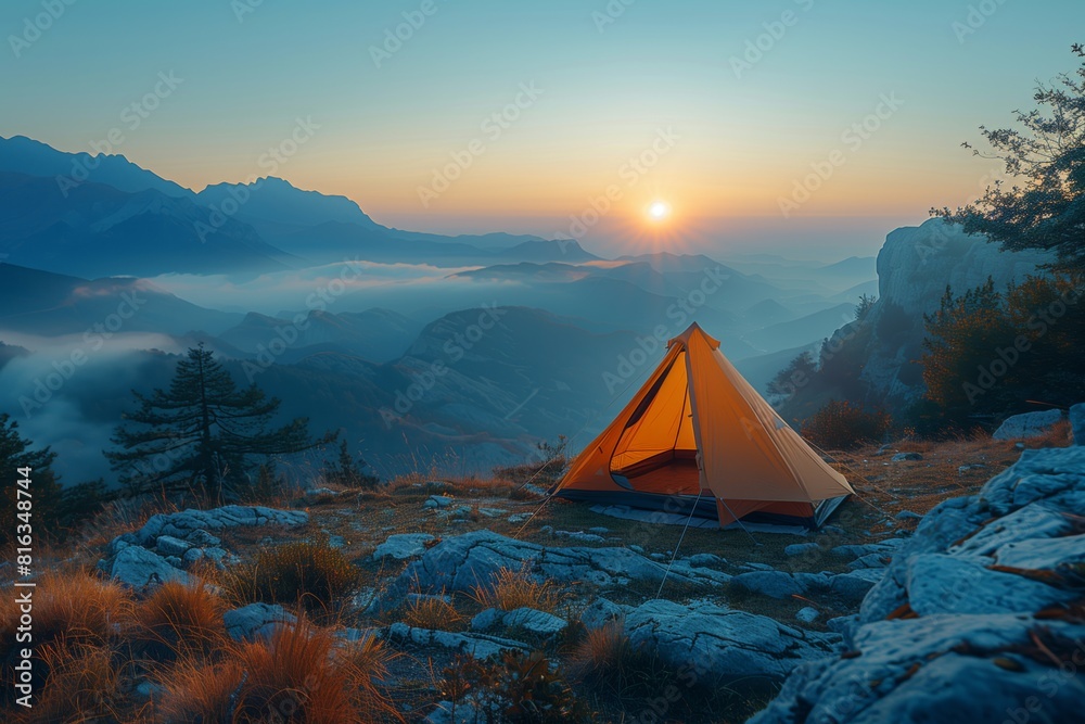 Camping tent on mountain ridge at sunrise with misty valleys