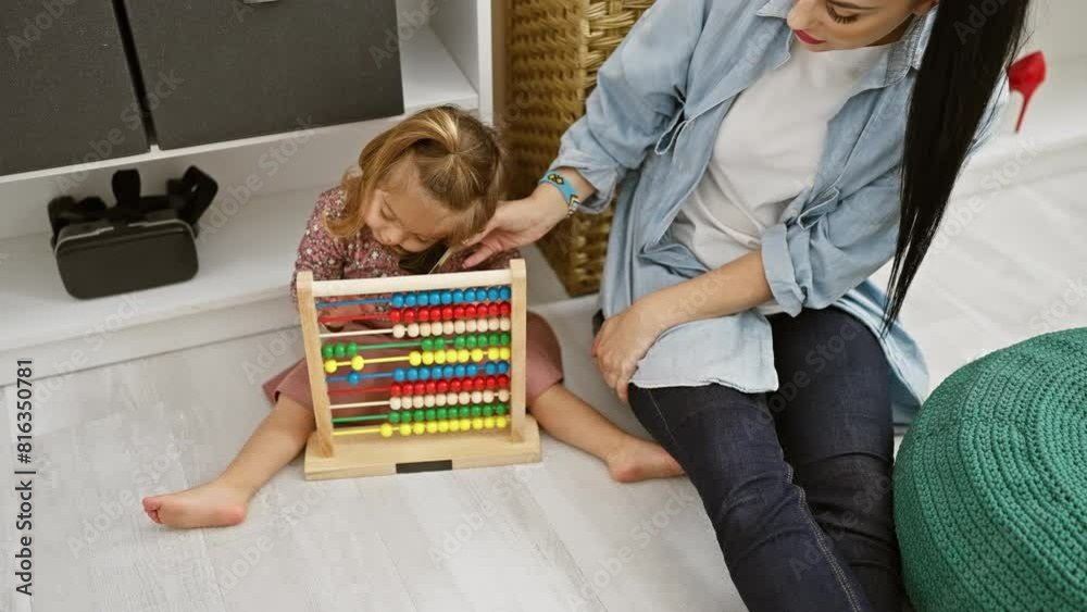 A woman in a denim shirt helps a young girl with an abacus in a contemporary room setting.