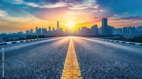 An empty asphalt road extends into a modern city skyline at sunset, offering a high-angle view that captures the urban scenery in a tranquil moment