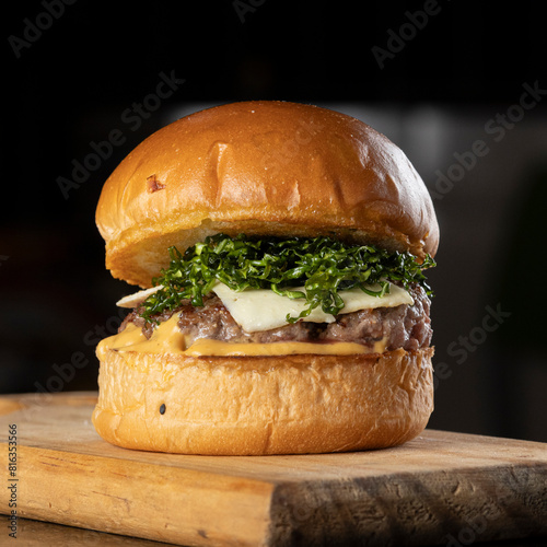 A big hamburger with brioche bread, meat, cheese, mustard sauce and crispy cabbage on a wooden table
