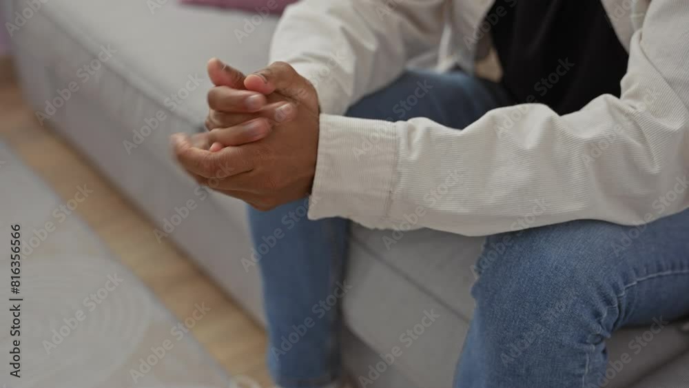 African american man in a casual outfit sitting with clasped hands on a couch indoors African american man in a casual outfit sitting with clasped hands on a couch indoors