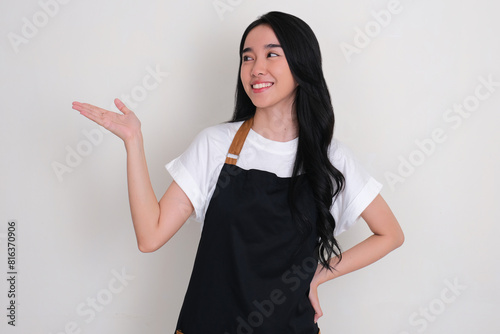 Asian woman wearing apron smiling and looking beside her with one hand presenting something photo