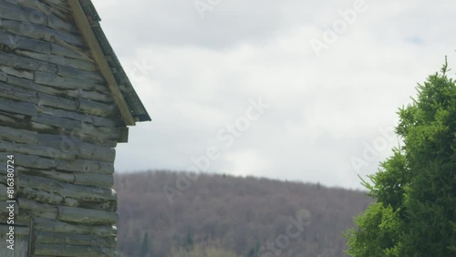 Time lapse cloud passing between shed house and coniferous tree with distant top hill