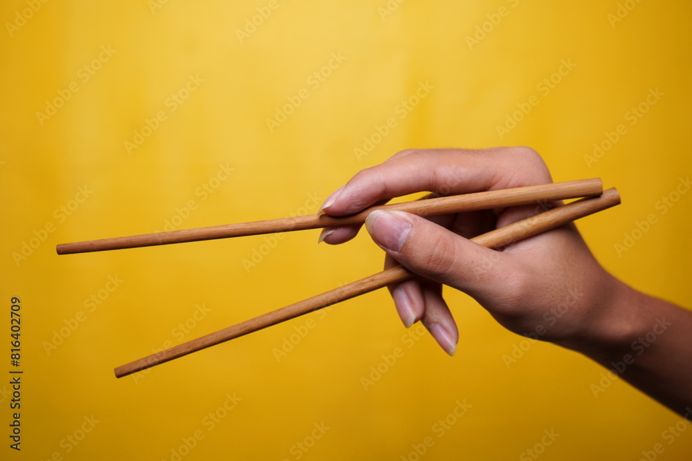 hand holding chopstick with isolated yellow background hand holding chopstick with isolated yellow background
