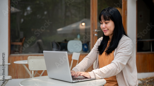 Photography A woman is working remotely at an outdoor table of a cafe, responding to emails on her laptop