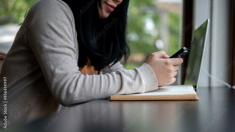 A cropped side view image of an Asian woman using her smartphone while sitting in a coffee shop. A cropped side view image of an Asian woman using her smartphone while sitting in a coffee shop.