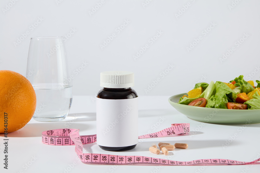 Photography from front view, some diet foods like vegetable salad, orange and fresh water, a blank medicine bottle for adding brand name. Mock up for promote, copy space Photography from front view, some diet foods like vegetable salad, orange and fresh water, a blank medicine bottle for adding brand name. Mock up for promote, copy space