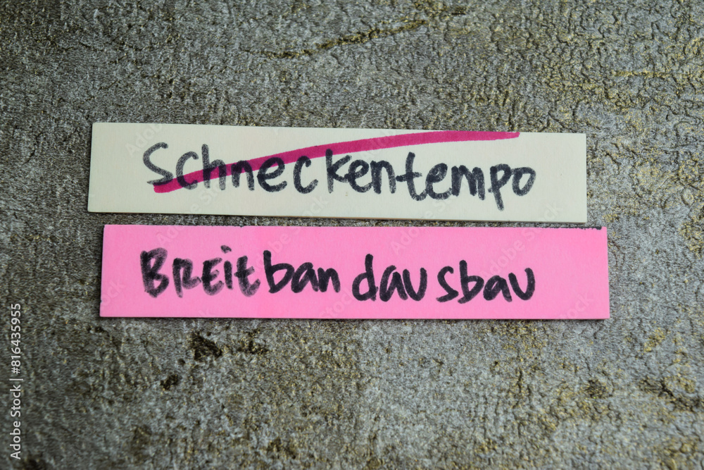 Concept of Learning language - German. Schneckentempo breitbandausbau it means Broadband expansion at a snail's pace written on sticky notes. German language isolated on Wooden Table.