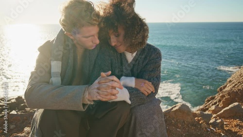 Affectionate lovers connecting hands sitting cliff at sea background closeup