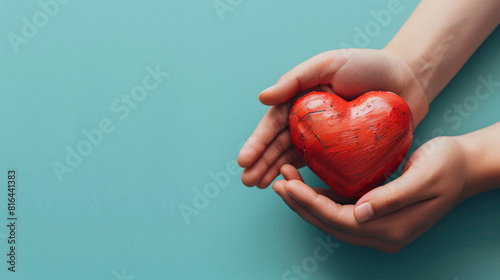 A pair of hands delicately cradles a bright red heart against a minimalist, solid-colored backdrop. The surreal quality and abundant copy space enhance the visual impact, ideal for themes of