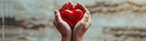 In a clean  minimalist composition  two hands hold a vivid red heart  set against a plain background. The unreal  striking appearance of the heart contrasts beautifully with the simplicity of the