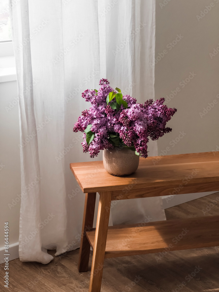 Fototapeta premium A bouquet of lilacs in a ceramic vase on a wooden oak bench in the living room