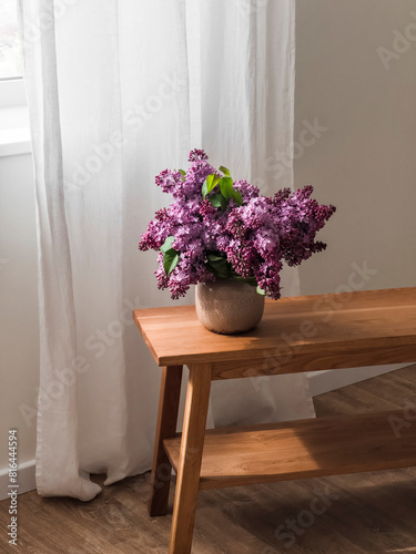 A bouquet of lilacs in a ceramic vase on a wooden oak bench in the living room