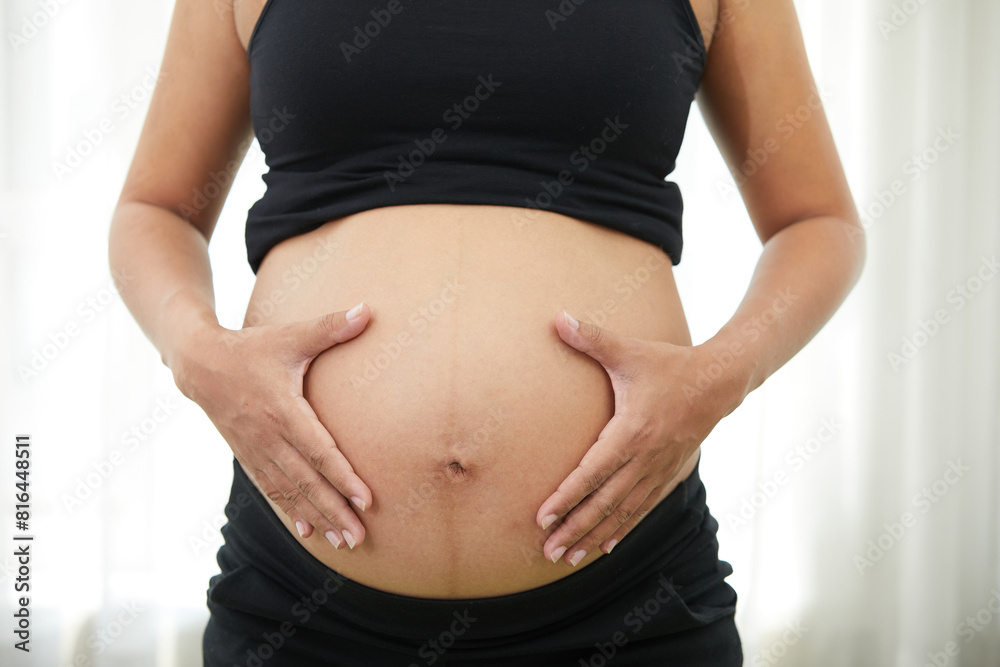 closeup pregnant woman holding hands on stomach closeup pregnant woman holding hands on stomach