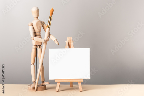 Creative composition with a miniature canvas on an easel and a wooden figurine of a man with a painting brush. Artistic creativity concept.