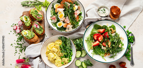 Fototapeta Naklejka Na Ścianę i Meble -  Spring fresh food with green leaf. Salads with strawberries, bacon and ravioli on light wooden background