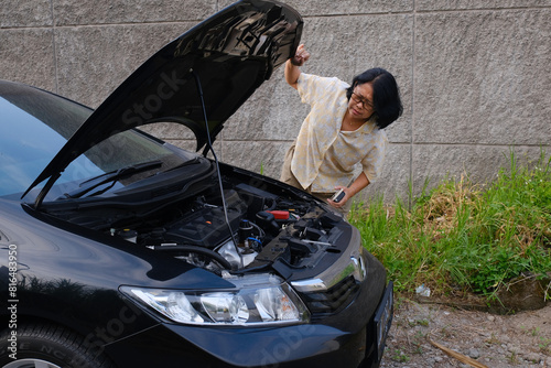 A woman was checking the engine of her broken down car parked on the side of the road photo