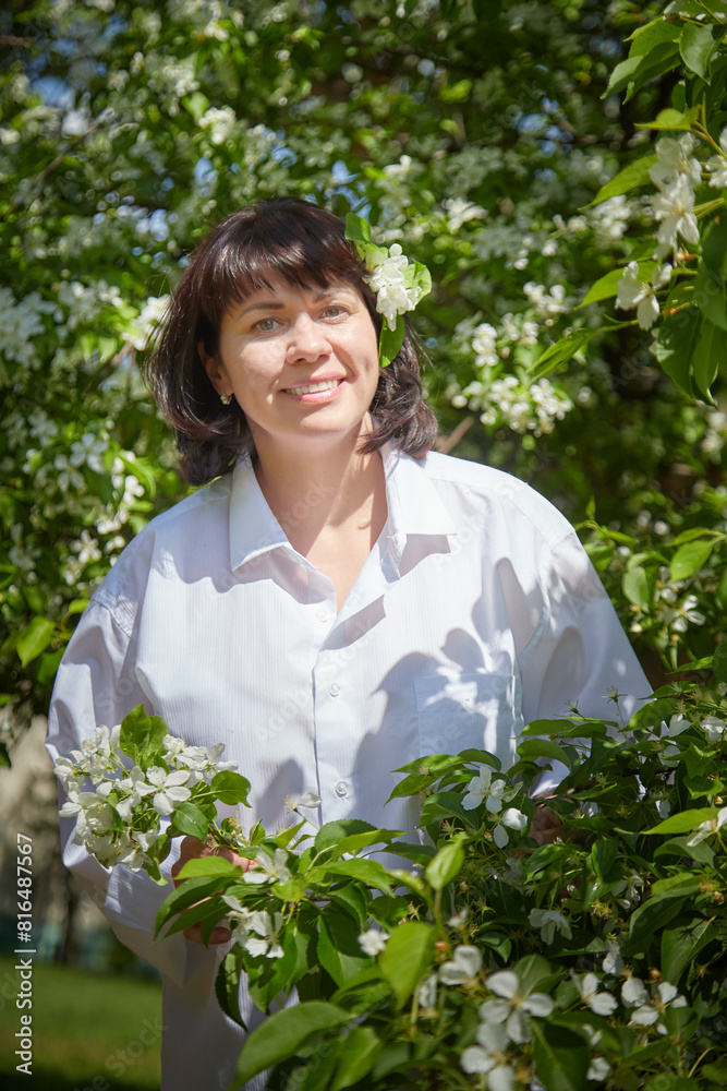 Girl walking and Relaxing near Blossoming apple Tree on Sunny Day. Portrait of Middle aged woman enjoying nature surrounded by white blossoms Girl walking and Relaxing near Blossoming apple Tree on Sunny Day. Portrait of Middle aged woman enjoying nature surrounded by white blossoms