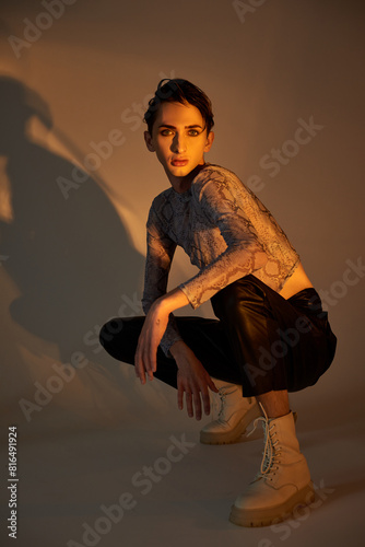 Konstfotografi A young queer person crouches in stylish attire against a white background, embodying pride