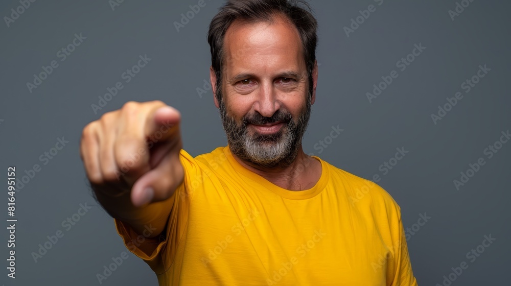  A man, dressed in a yellow T-shirt, smiles and gestures at the camera with an uplifted hand