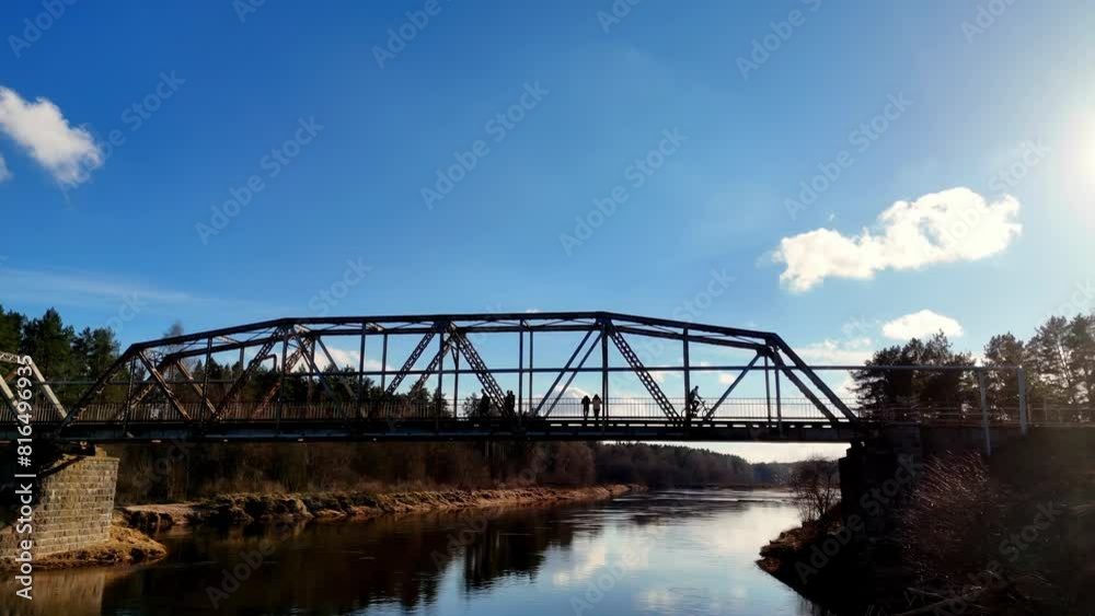 People cross Latvian waterway bridge contrasted clouds above river water shine People cross Latvian waterway bridge contrasted clouds above river water shine