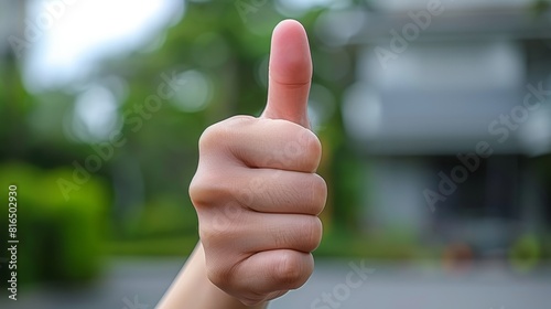  A hand giving a thumbs-up in sharp focus against a softly blurred building backdrop