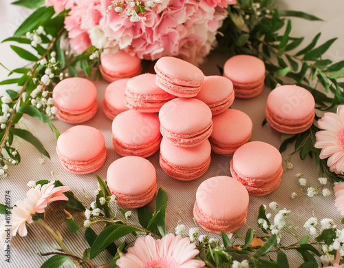 Sweet pink macarons or macaroons and flowers on wooden table