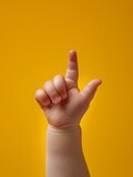The hand of a small child shows one finger up. A small baby hand on a yellow background.