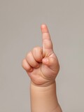 The hand of a small child shows one finger up. A small baby hand on a grey background.
