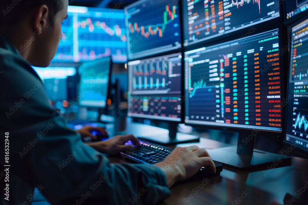 A man is sitting in front of a computer monitor with multiple screens displaying financial data. He is typing on a keyboard, possibly working on a financial report or analyzing market trends A man is sitting in front of a computer monitor with multiple screens displaying financial data. He is typing on a keyboard, possibly working on a financial report or analyzing market trends