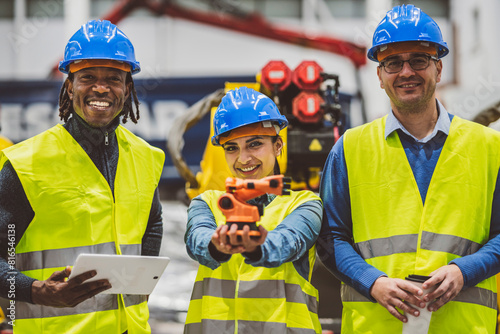Diverse team of engineers smiling and holding a robotic arm prototype in an industrial facility.