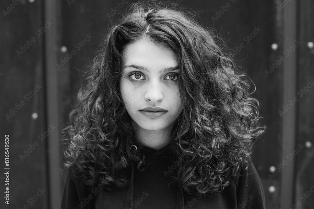 White brunette teenage girl with curly hair poses on the street in the city.