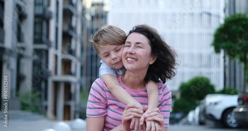 Outdoor family day concept. Portrait of adorable caucasian brunette mother sitting and kid son hugging her from the back