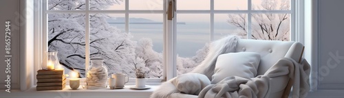 A cozy armchair sits in front of a window. The window is covered in snow. There are candles and a book on the windowsill.