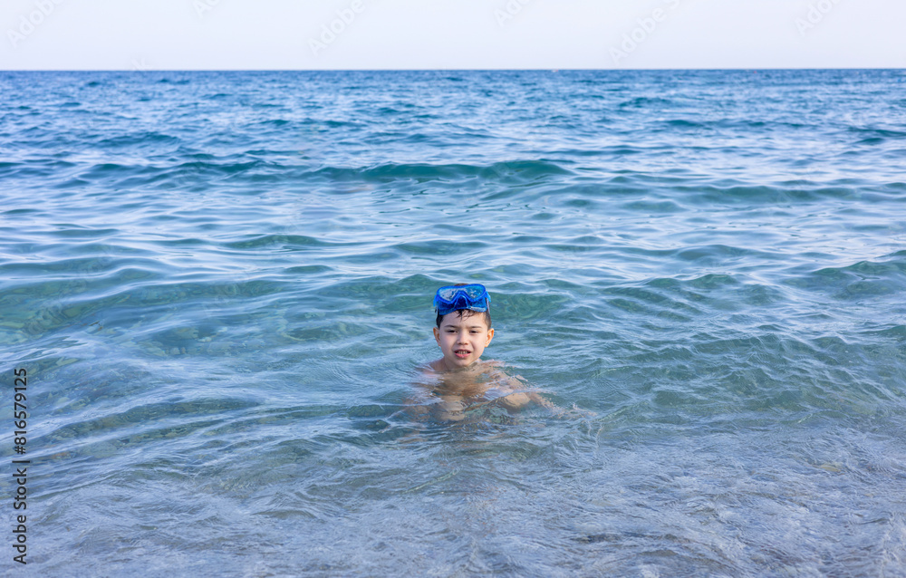 cute kid with hat on beach against sea or is having fun in summer vacation.boy with snorkel, diving set on eyes. child sprinkle with water, swimming, playing with boat ship toy, digging tools, bucket.