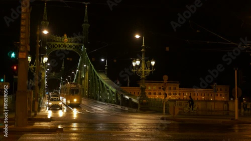 Tram transport on liberty bridge at night. A view of tram transport and cars driving across the street by Freedom bridge against night sky in Budapest.